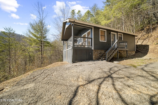 view of front of home featuring covered porch, driveway, stairway, and a view of trees