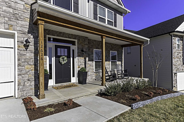 view of exterior entry featuring board and batten siding, covered porch, stone siding, and a garage