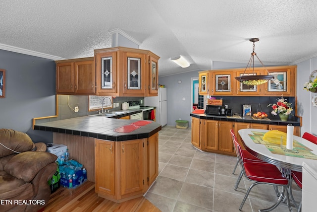 kitchen with decorative light fixtures, a sink, tile counters, brown cabinetry, and glass insert cabinets