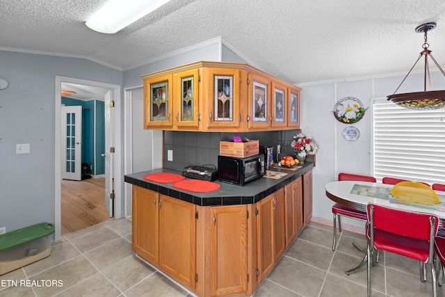 kitchen featuring brown cabinetry, lofted ceiling, glass insert cabinets, decorative light fixtures, and black microwave