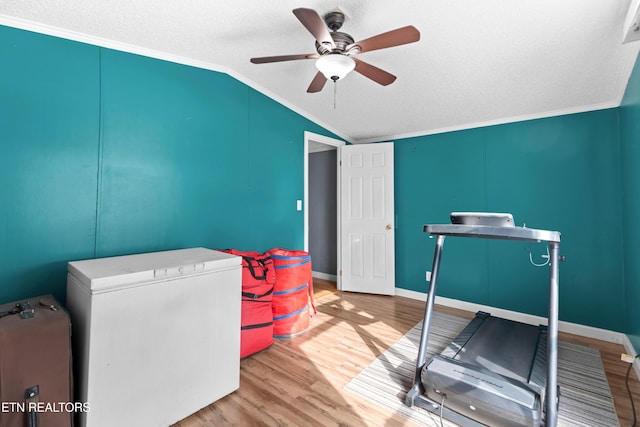 exercise room featuring a ceiling fan, wood finished floors, vaulted ceiling, crown molding, and a textured ceiling