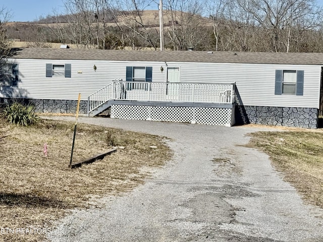 manufactured / mobile home with a shingled roof, gravel driveway, and a deck