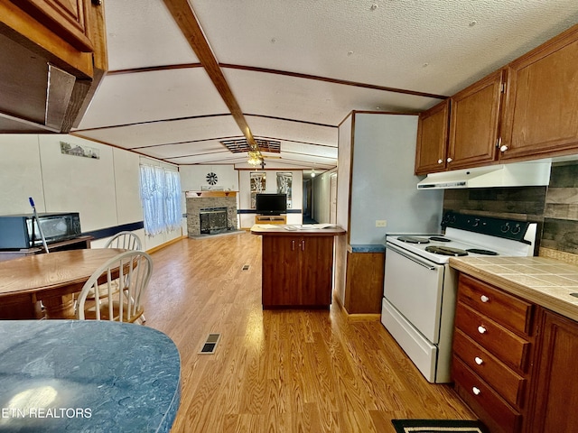 kitchen with electric stove, a glass covered fireplace, tile countertops, light wood-type flooring, and under cabinet range hood