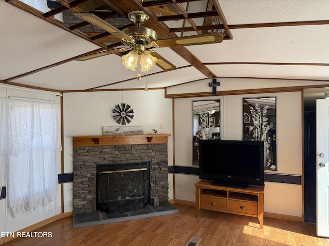 living room with vaulted ceiling with beams, ceiling fan, a stone fireplace, baseboards, and light wood-style floors