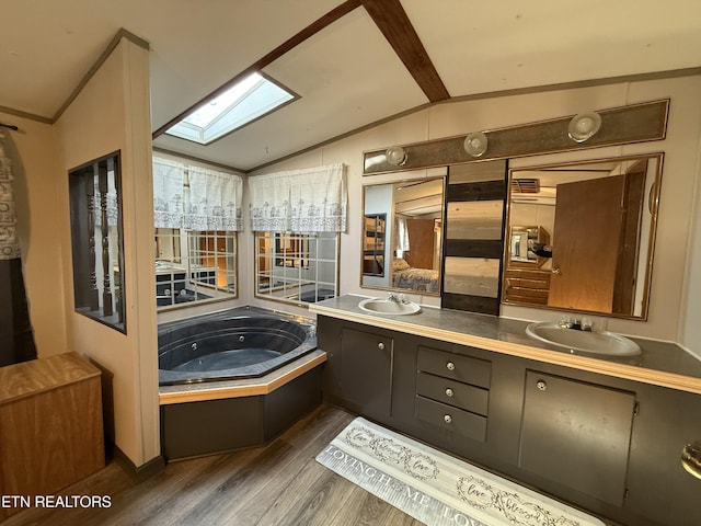 bathroom with vaulted ceiling with skylight, wood finished floors, a sink, a whirlpool tub, and double vanity