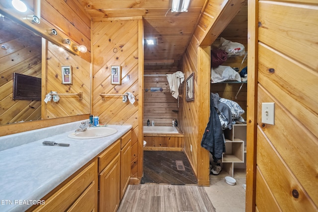 bathroom featuring wood walls, vanity, wood finished floors, wooden ceiling, and a bath