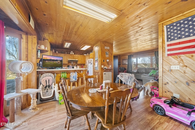 dining area featuring light wood-type flooring, wood ceiling, and wooden walls