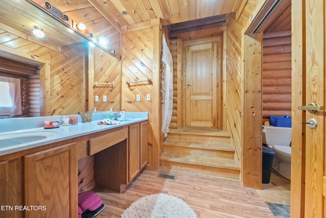 bathroom featuring toilet, wood finished floors, wood ceiling, log walls, and double vanity