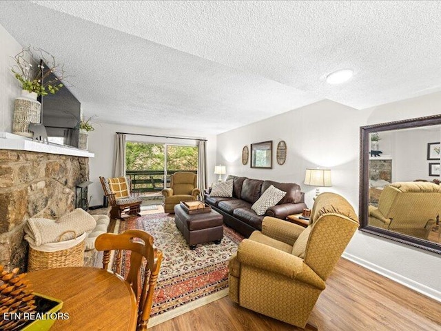 living area with a textured ceiling, wood finished floors, and a stone fireplace