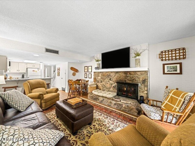 living area featuring visible vents, a stone fireplace, and a textured ceiling