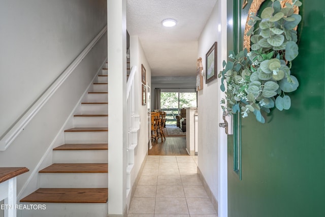 interior space featuring a textured ceiling, light tile patterned floors, baseboards, and stairway