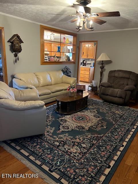 living room with ornamental molding, ceiling fan, a textured ceiling, and wood finished floors