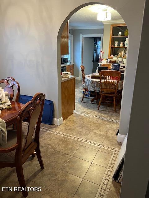 dining space featuring arched walkways, tile patterned flooring, crown molding, and baseboards