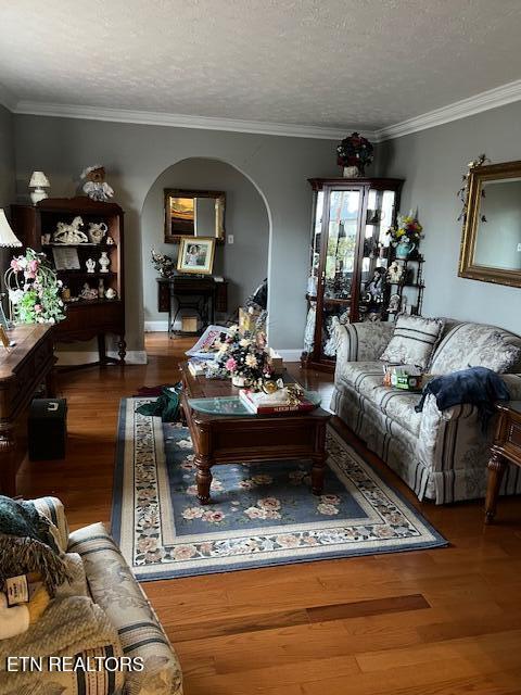 living area with arched walkways, crown molding, a textured ceiling, and wood finished floors