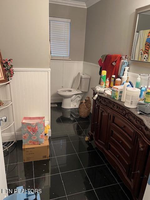 bathroom featuring ornamental molding, a wainscoted wall, toilet, and tile patterned floors