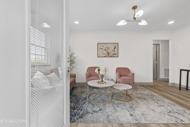 living area featuring an inviting chandelier, crown molding, wood finished floors, and visible vents