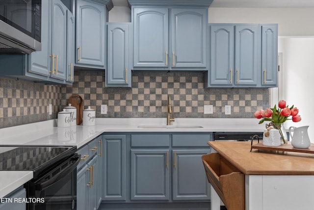 kitchen with blue cabinetry, stainless steel microwave, a sink, light countertops, and decorative backsplash