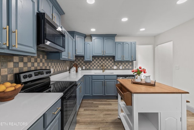 kitchen featuring a sink, light wood-style floors, appliances with stainless steel finishes, blue cabinets, and tasteful backsplash