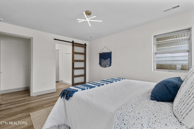 bedroom featuring visible vents, a barn door, baseboards, and wood finished floors