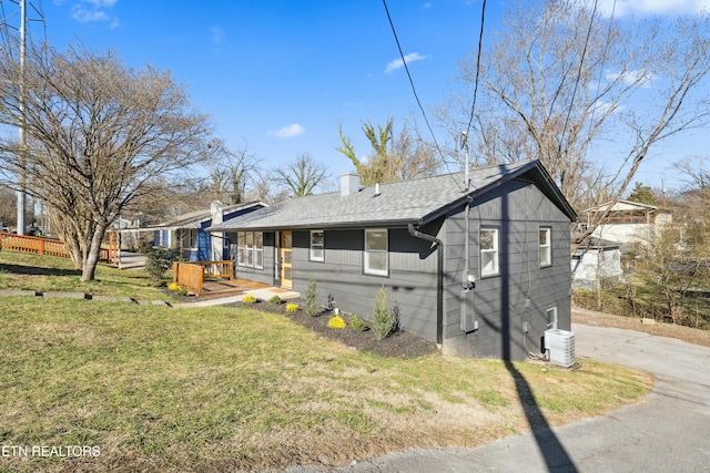 exterior space featuring central AC, a shingled roof, driveway, a lawn, and a chimney