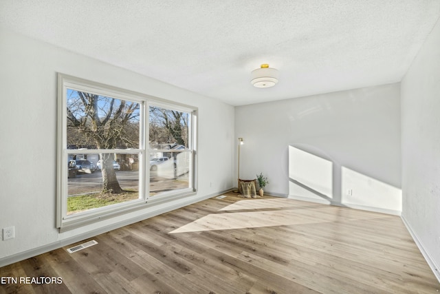 empty room featuring visible vents, baseboards, a textured ceiling, and wood finished floors