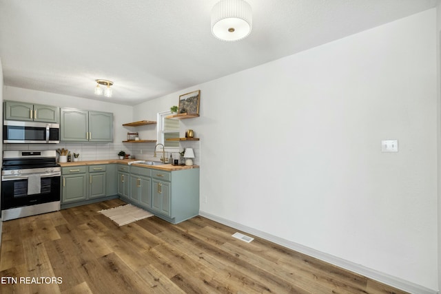 kitchen featuring butcher block counters, light wood-type flooring, decorative backsplash, stainless steel appliances, and open shelves