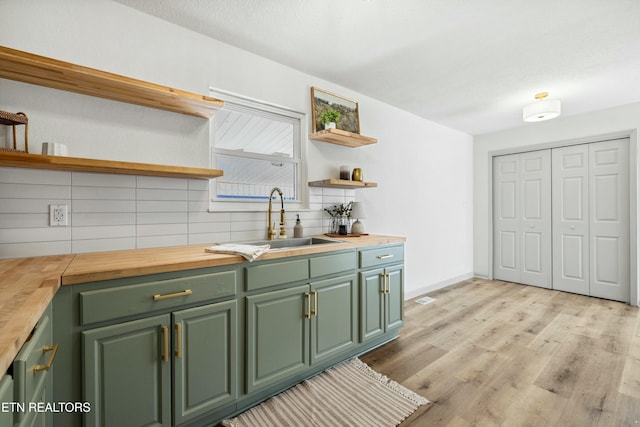 kitchen with open shelves, green cabinets, butcher block counters, and a sink