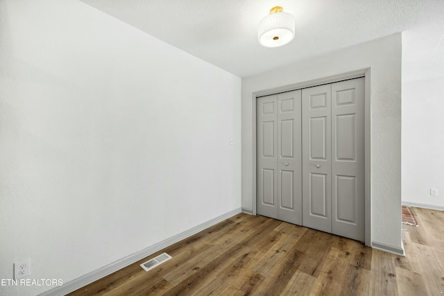 unfurnished bedroom with a closet, visible vents, baseboards, and wood finished floors