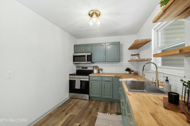 kitchen featuring a sink, open shelves, appliances with stainless steel finishes, butcher block counters, and green cabinetry