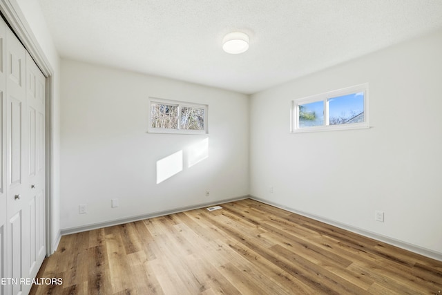 unfurnished bedroom featuring a closet, light wood-style flooring, a textured ceiling, and baseboards