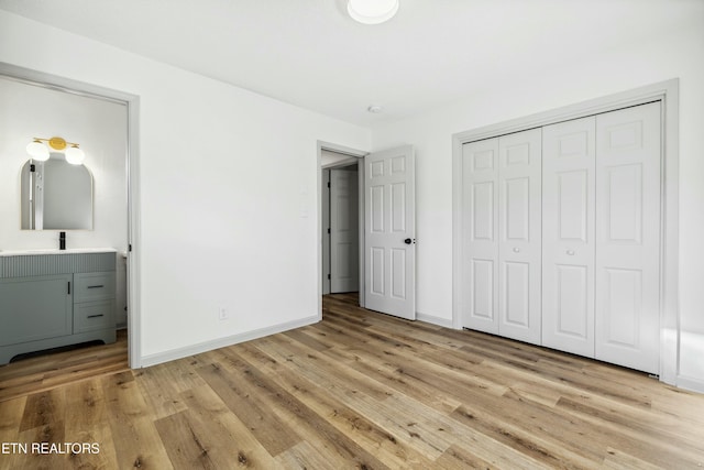 unfurnished bedroom with connected bathroom, baseboards, a closet, and light wood finished floors