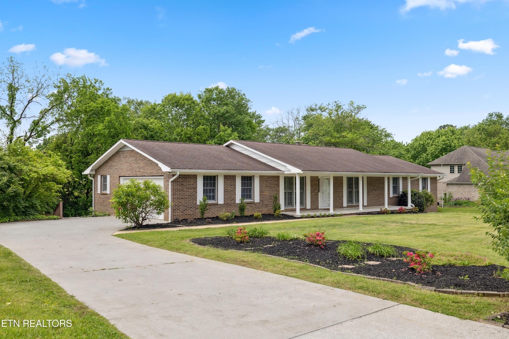 ranch-style house with a garage, a front lawn, covered porch, brick siding, and driveway