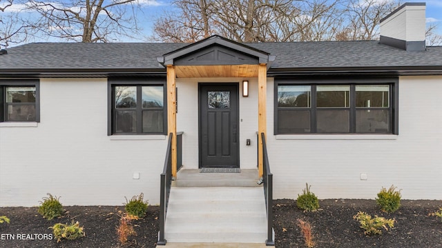 property entrance with brick siding, a chimney, and a shingled roof