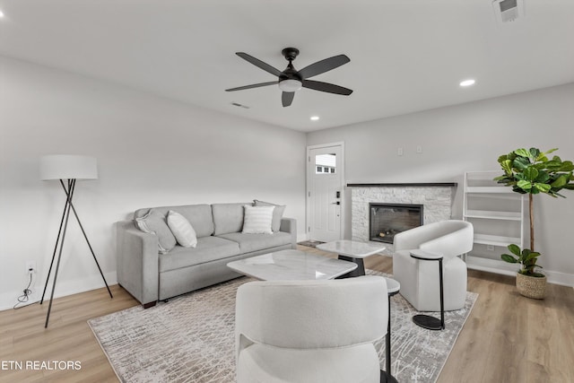 living room with visible vents, a stone fireplace, light wood-type flooring, and baseboards