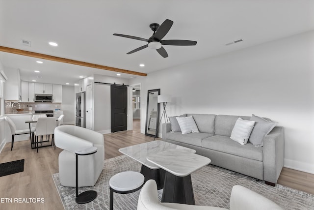 living area featuring a ceiling fan, visible vents, light wood-style floors, a barn door, and beamed ceiling