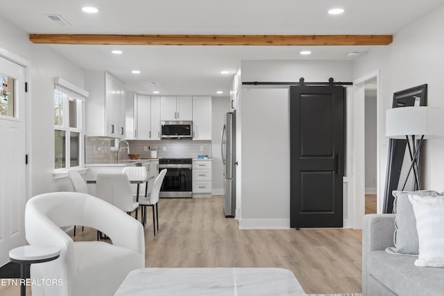 kitchen featuring beam ceiling, white cabinets, appliances with stainless steel finishes, and a barn door