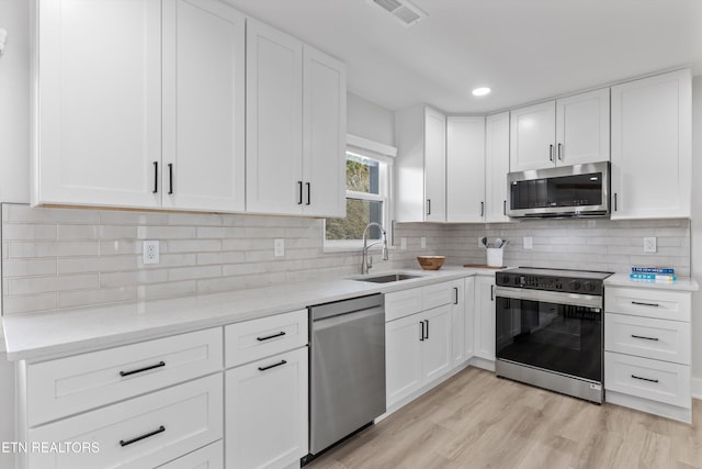 kitchen with visible vents, light wood-style flooring, a sink, tasteful backsplash, and stainless steel appliances