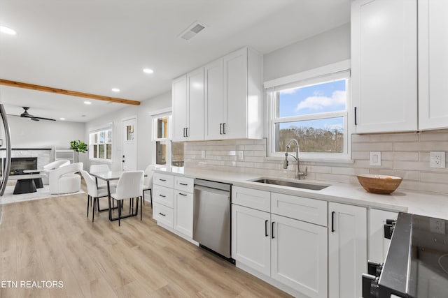 kitchen with light wood-style flooring, a sink, white cabinetry, a fireplace, and dishwasher