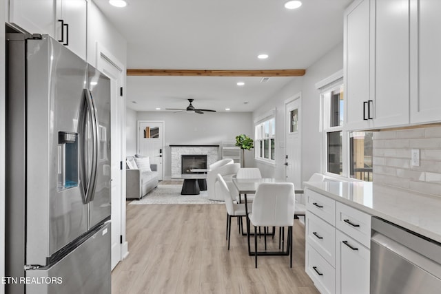 kitchen featuring tasteful backsplash, light wood-style floors, appliances with stainless steel finishes, white cabinets, and a fireplace