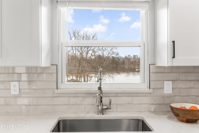 interior details with decorative backsplash, light stone countertops, white cabinetry, and a sink