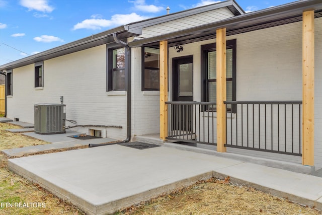 entrance to property featuring a patio, brick siding, and central AC unit