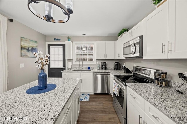 kitchen featuring light stone counters, a sink, white cabinets, appliances with stainless steel finishes, and pendant lighting