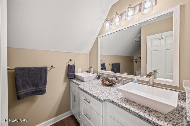 full bath with vaulted ceiling, double vanity, a sink, and baseboards