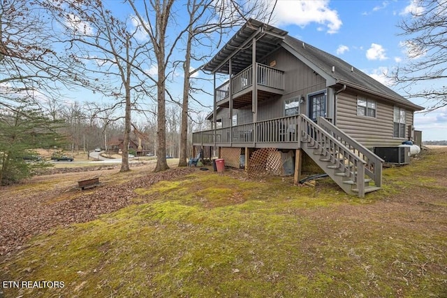 back of property with a balcony, central air condition unit, stairs, a yard, and faux log siding