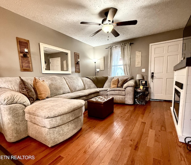 living room featuring a glass covered fireplace, hardwood / wood-style flooring, a textured ceiling, and ceiling fan