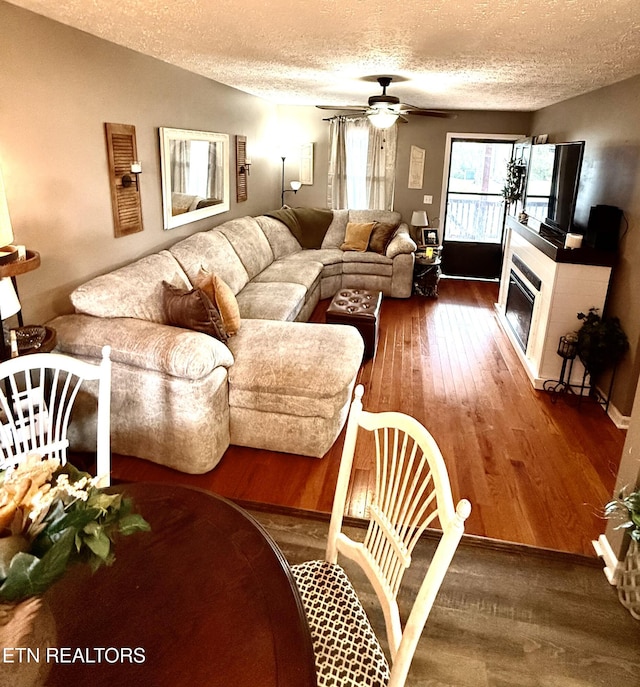 living room with ceiling fan, wood finished floors, a textured ceiling, and a glass covered fireplace