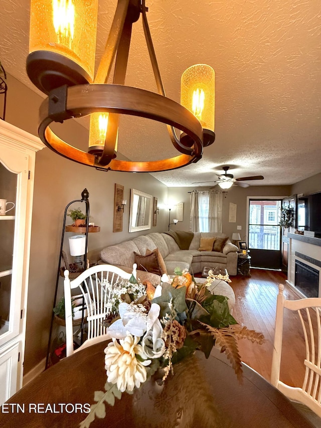 dining area with hardwood / wood-style floors, a textured ceiling, a glass covered fireplace, and a ceiling fan