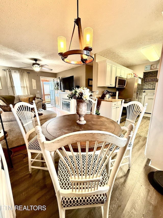 dining room with ceiling fan with notable chandelier, a textured ceiling, washer / clothes dryer, and wood finished floors