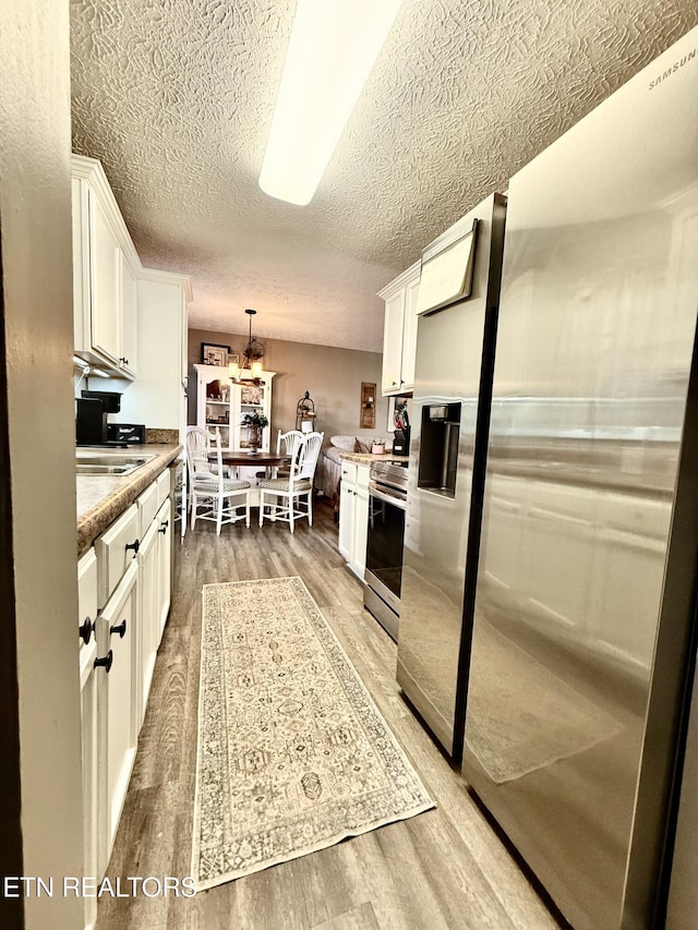 kitchen with light wood-type flooring, stainless steel appliances, and white cabinets