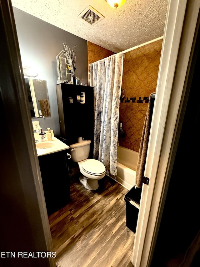 full bath featuring visible vents, toilet, vanity, wood finished floors, and a textured ceiling